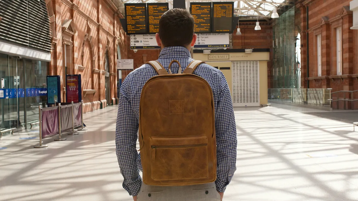 Man wearing brown leather backpack standing inside a train station