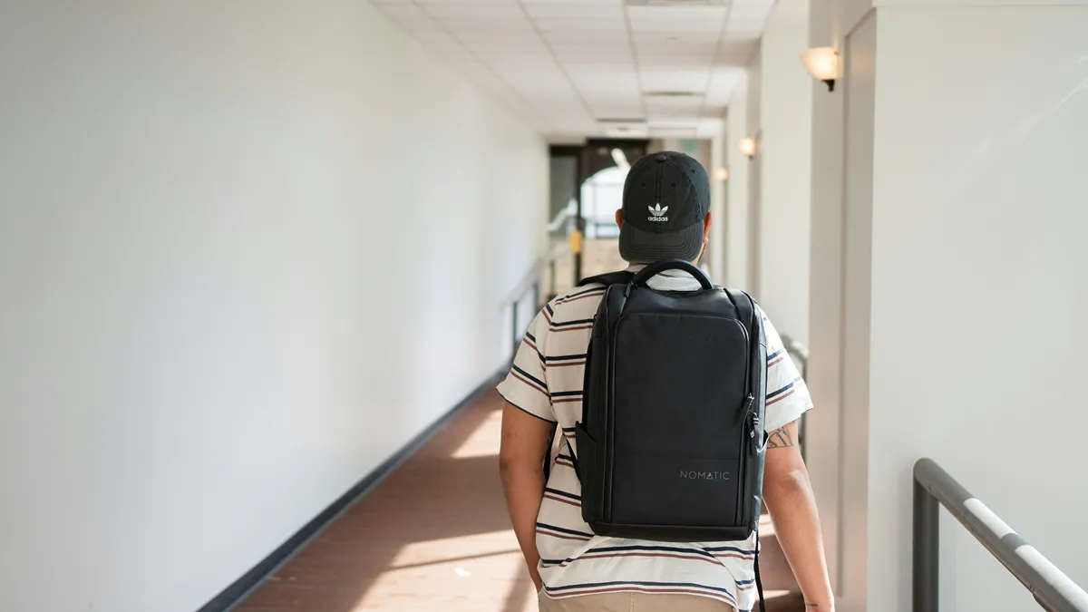 Person wearing black backpack walking down a bright building hallway.